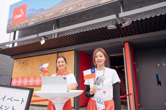 Dos mujeres con bandera chilena dan la bienvenida al pabellón de Chile en Osaka, Japón
